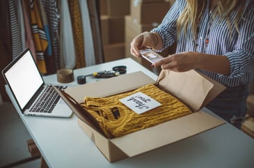 Woman packing a sweater she recently sold to be mailed to the new owner. 