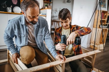 A man and young boy work with power tools on a building project. 