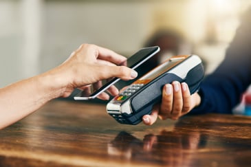 Closeup of a person using their cell phone to pay using tap at a terminal