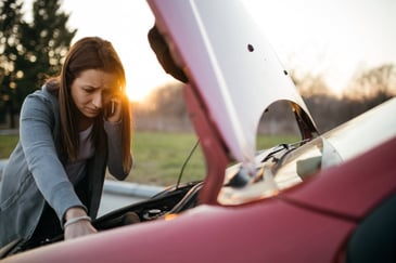 A woman looks under the hood of her car while talking on the phone