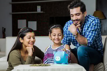 Parents watch their daughter put money into a piggy bank