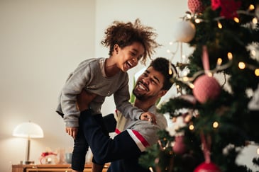 A young father and daughter laugh by a Christmas tree