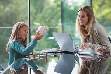 A mother and daughter discuss finances together with a piggy bank and laptop
