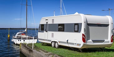 An RV by the water with a boat in front of it