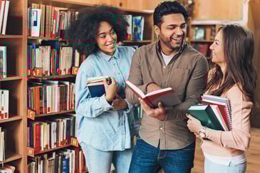 Three college students talk in the library while holding books
