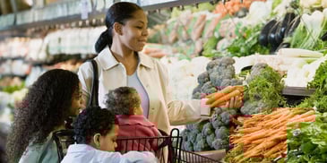 A mother of three shopping in the grocery store's produce section holding carrots