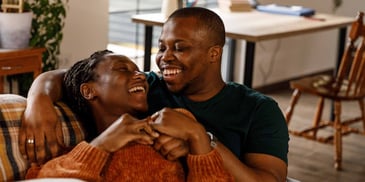 A young couple smiles and holds each other on the sofa in their home