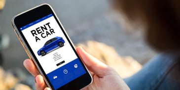 An outstretched hand holds a phone, displaying an advertisement for renting a car