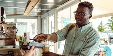 A gentleman uses his phone to pay for a coffee in a coffee shop