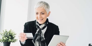 A woman holds out a credit card in one hand and a tablet in the other