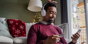 A man wearing headphones and sitting in his decorated living room, making an online purchase