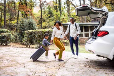 A family loads suitcases into the car for a road trip
