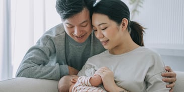 A mother and father look down at their newborn baby, smiling, who is in the mother's arms