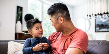 A father sits holding his young, smiling son