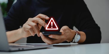 Hands holding a mobile device with a security warning appearing above in red