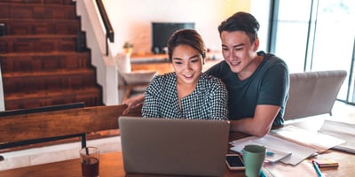 A couple sits at a table with a laptop out, looking at the screen