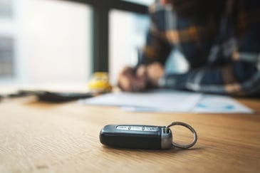 A car key sits on a table as an individual works at the table
