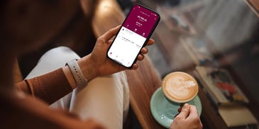 Two outstretched hands, with one holding a latte and the other holding a mobile phone, showing a banking app with an outstanding loan balance