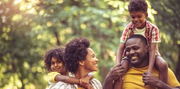 A young family walking in nature, with the children on their parents' shoulders