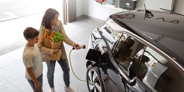 A mother and her son standing in their garage with groceries, preparing to plug in their EV