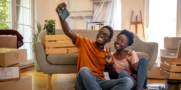 A young couple sitting on the floor of their new home, smiling and taking a photo