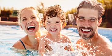 An adult couple smile in a pool with their smiling young child