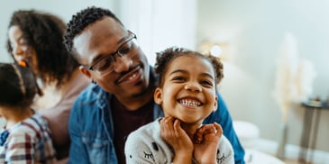 A young girl looks up and smiles, as her father looks upon her proudly