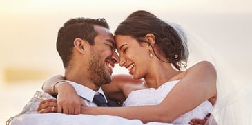A groom holds up a bride, with their faces together and smiling at each other