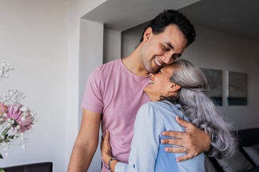 An adult son smiles and hugs his mother closely