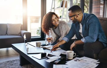 A young couple sits on the sofa in their living room, doing finances at their coffee table