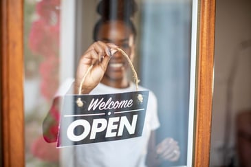 A woman puts an open welcome sign on her small business's door