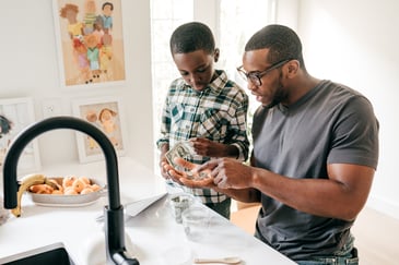 A father teaches his son about money while standing in their kitchen