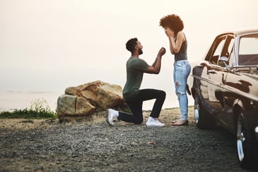 A young man one on knee proposing by a lake shore