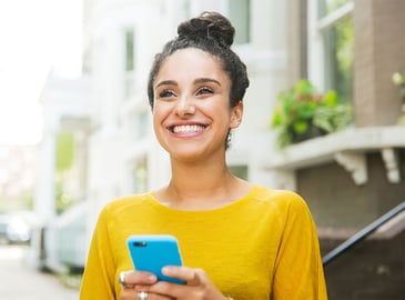 A young woman smiles while holding her smart phone.