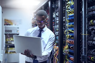 A man standing in a server room with a laptop