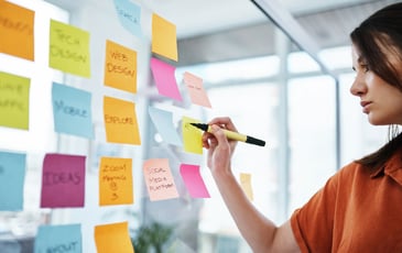 Close up of an employee writing on a sticky note on an inspiration wall