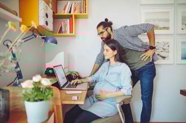 Pregnant woman and her partner using a laptop at a desk