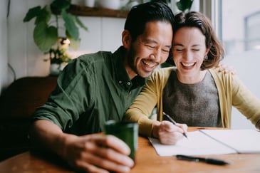 a young couple laughs together while managing their finances