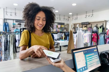A young woman pays at a terminal using her smart phone's contactless mobile wallet.