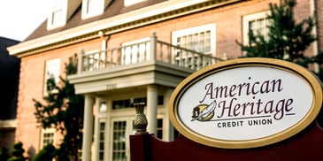 Exterior of American Heritage Credit Union, with the logo on a sign close-up to frame