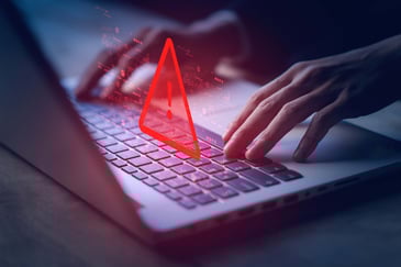Close-up of hands typing on a keyboard while a red caution symbol floats above.
