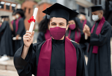 A graduate wearing a mask holds up his diploma