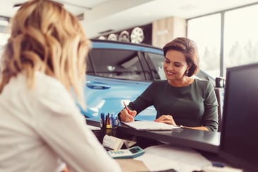 A woman signing paperwork at the car dealership