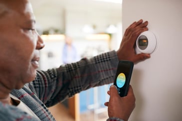 A homeowner checks the temperature using their thermostat and a back up on their phone.