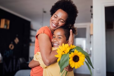 a mother hugs her young daughter after being given a bouquet of sunflowers