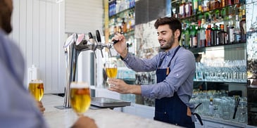 A young bartender pouring a drink behind a bar for a customer
