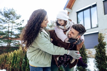 Parents and their young daughter play in their yard, dressed warm for winter.