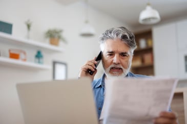 A concerned man calls his financial institution while reviewing his credit card statements.
