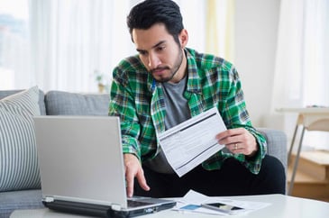 A man looks at his laptop while holding his credit card paperwork.