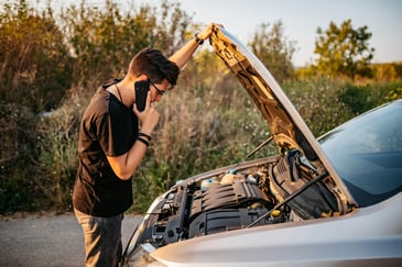 Young man on the phone seeking advice or help from car technician while holding the hold up looking at the engine issue.